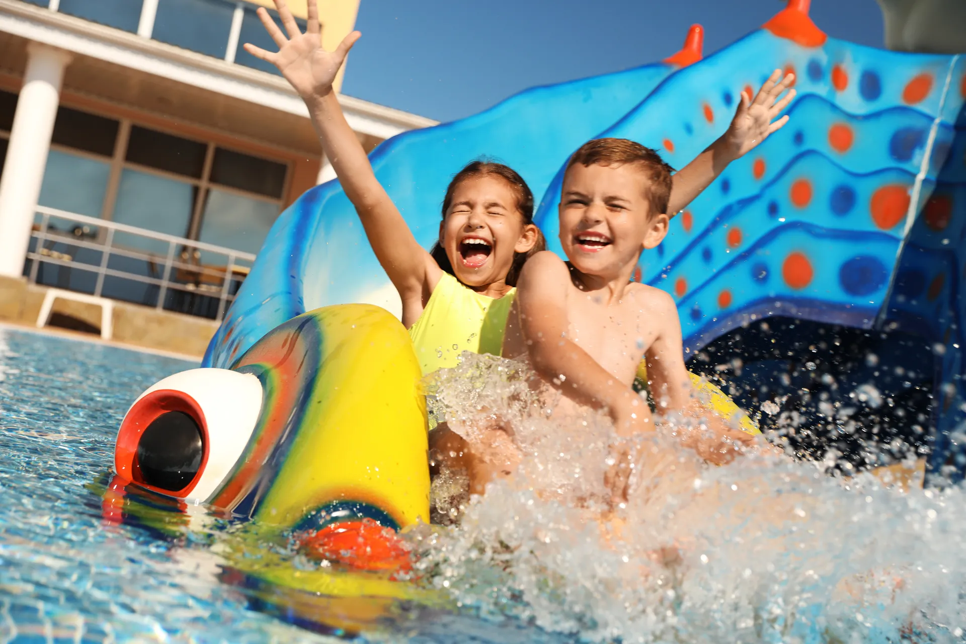 Zwei Kinder rutschen auf einer bunten Wasserrutsche in ein Kinderbecken