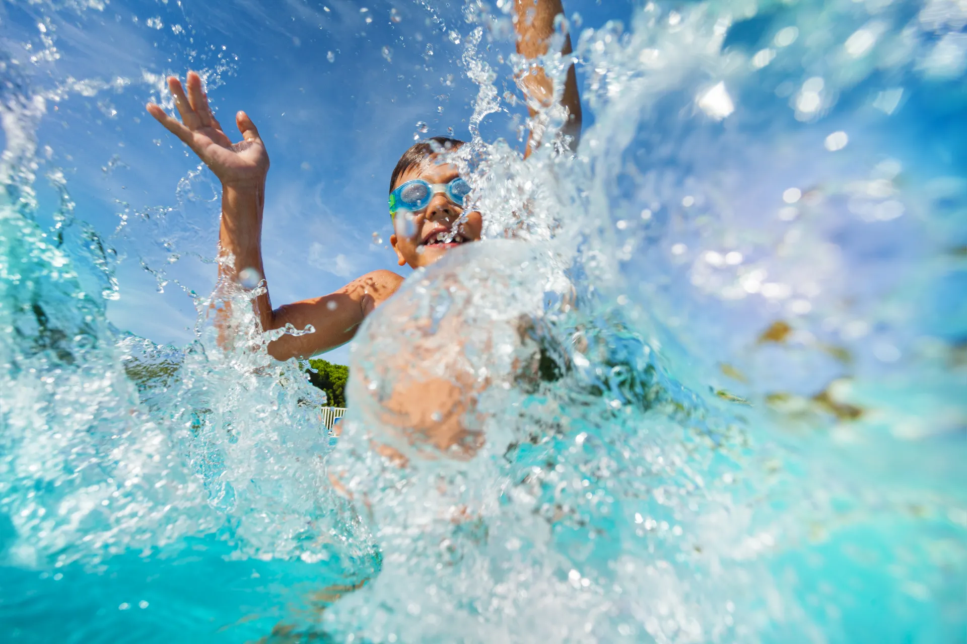 Ein Junge plantscht unter freiem Himmel in klarem Wasser mit einer Schwimmbrille